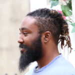 a side profile of malik smiling and wearing braided locs.